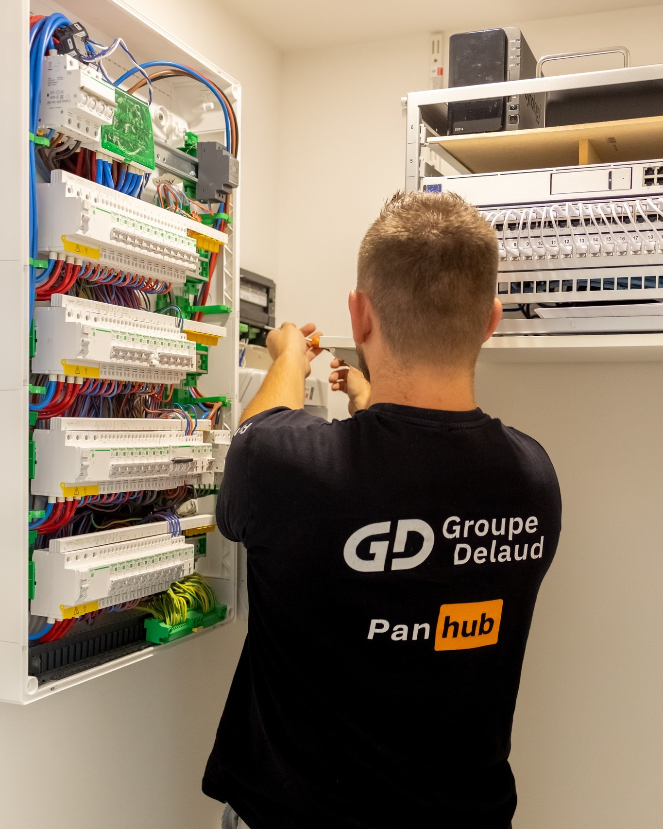 Ouvrier avec un t-shirt Groupe Delaud en train de faire des branchements électriques sur un panneau électrique neuf